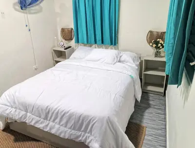 a bedroom with a bed with white sheets and blue curtains at Habitacion cerca de la Playa in Boca Chica