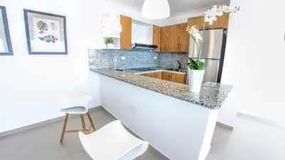 a kitchen with a granite counter top and white chairs at Vista Marina Residence in Boca Chica