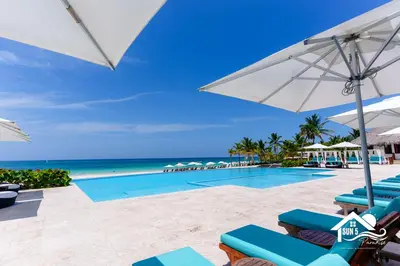 a pool with chairs and umbrellas and the ocean at Vista Family Garden Suite Pool front 2 Bdrms in Punta Cana
