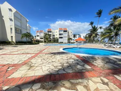 a resort swimming pool with palm trees and buildings at comfortable apartment in La Puntica de Juan Dolio