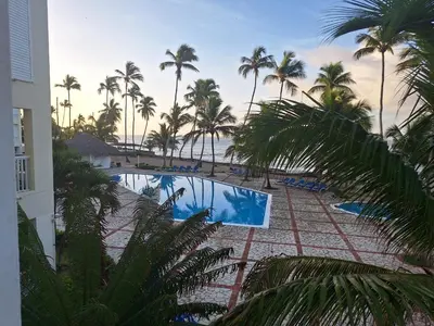 a view of a pool with palm trees and the ocean at marina view in La Puntica de Juan Dolio