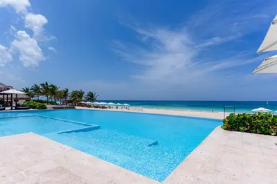 a swimming pool next to a beach with an umbrella at Aqua Fam Swim out Suite - Pool @ Cana Rock G 117 in Punta Cana