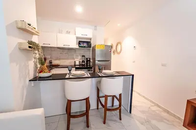 a kitchen with a black counter and two white bar stools at Directo piscina jardín terraza @ Cana Rock in Punta Cana