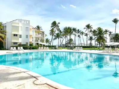 a large swimming pool with palm trees in the background at Playa Privada | Terraza & Piscina • WiFi Rápido in Punta Cana