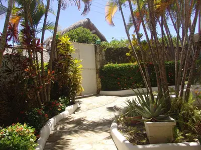 a garden with palm trees and a white fence at Waverider Apartments in Cabarete