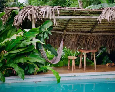 a thatch roofed hut with a table and chair next to a pool at Ganesh Village Community in Colorado