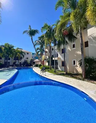 a large swimming pool with palm trees in front of a building at Apartamento Rosa Hermosa in Punta Cana