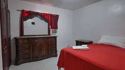 a bedroom with a dresser with a mirror and a red bed at Garden Mar in Bonao
