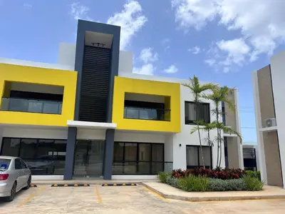 a yellow and white building with a car parked in a parking lot at jardines de caleta 7 in La Romana