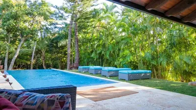 a swimming pool with blue lounge chairs and trees at Chic Villa Pool Casa de Campo in La Romana