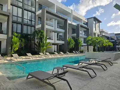 a swimming pool with chaise lounge chairs in front of a building at Apartamento a estrenar con acceso privado a la playa in Punta Cana