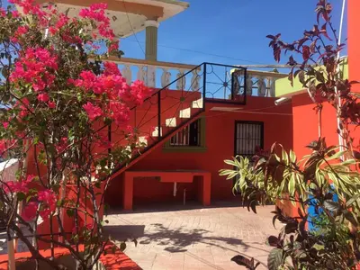 a red building with a staircase and pink flowers at Hotel Pensión la Hermosa Barahona in Santa Cruz de Barahona