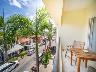 a balcony with a wooden table and a palm tree at Plaza Achim 2BR APT heart of nightlife area in Sosúa