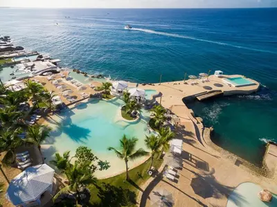 an aerial view of a pool with palm trees and the ocean at Luxury Penthouse with roof top & infinitive pool ocean view in Tracadero Beach Club in Bayahibe
