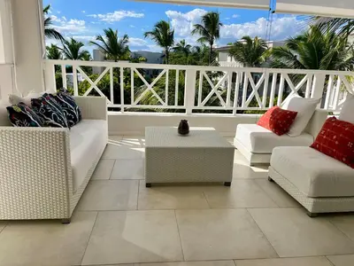 a living room with couches and a balcony with palm trees at Luxury Penthouse with roof top & infinitive pool ocean view in Tracadero Beach Club in Bayahibe