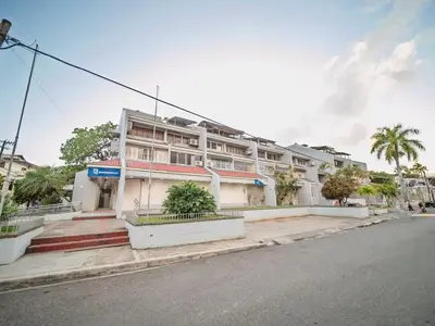 a large white building with palm trees in front of it at Central 1BR APT - 1 minute Walking from Rumba in Sosúa