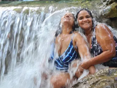 two people sitting on rocks in front of a waterfall at 2 Bdrm, 1 Bath, Wifi, Near River and Beach, 3R in Paraíso