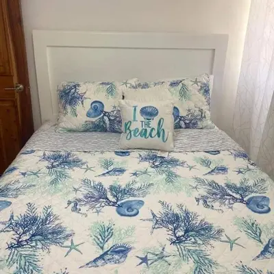 a bed with a blue and white comforter with a i the beach pillow at Casita Linda Playas Rios Wifi Agua HOT AC and more in Paraíso