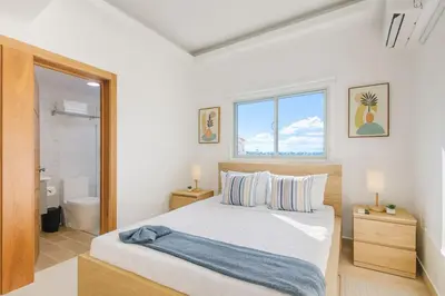 a white bedroom with a bed and a bathroom at Cozy 3BR Condo in Ens. Ozama in La Cruz de Mendoza