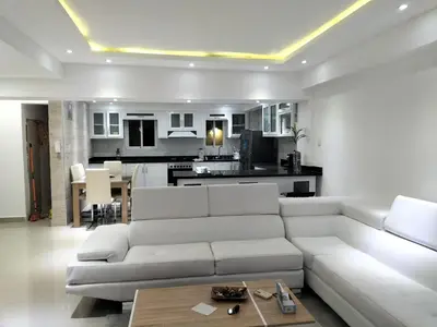 a living room with a white couch and a kitchen at Apartamento con tres habitaciones, piscina y parking techado gratis in Juan López