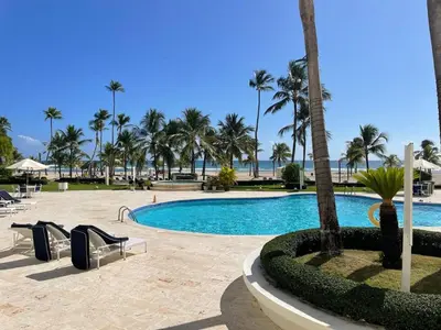 a swimming pool with palm trees and a beach at Oceanfront apartment with views and pool in Los Corrales