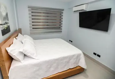 a bedroom with a bed with white sheets and a flat screen tv at Hermoso Alojamiento con Terraza y Jacuzzi en Santiago in Santiago de los Caballeros