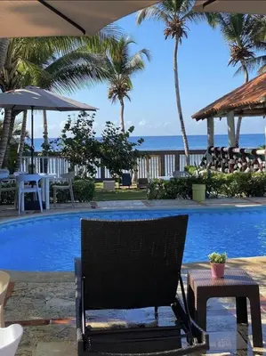 a chair next to a swimming pool with palm trees at El Mar Azul Franchecis hostal in Juan Dolio