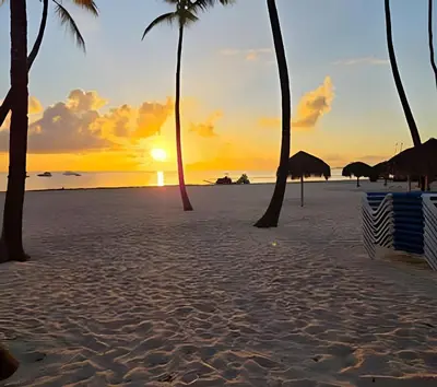 a sunset on a beach with palm trees at Los Corales Moderno Apto: Piscina y Playa 10 min in Punta Cana