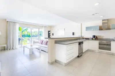 a kitchen with white cabinets and a living room at Iberostate 2BR Apartment - BBQ, Terrace, Lake & Golf Views, Beach Club Access in Punta Cana