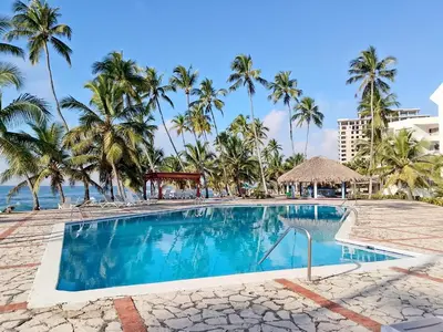 a swimming pool with palm trees and the ocean at Residencias Turísticas Espinosa in Villas del Mar