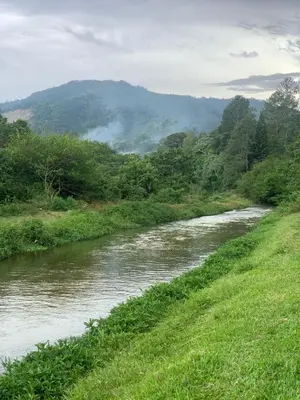 a river next to a grassy field with a mountain at Villa 3 Habitaciones con piscina in Jarabacoa