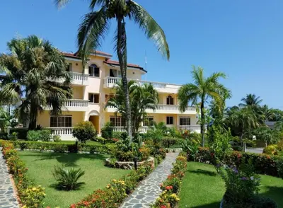 a large yellow building with palm trees and a garden at Casa Lio in Boca Chica
