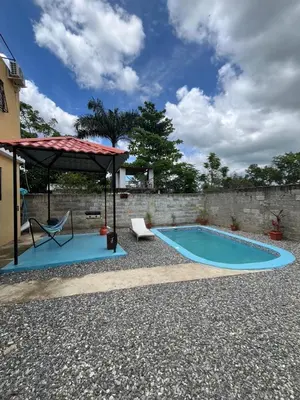 a swimming pool with a umbrella and a table and a chair at Pequeña villa de María in Villa Mella
