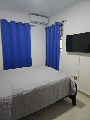 a bedroom with a bed with blue curtains and a tv at Naime 3 Bristol villa in San Pedro de Macorís