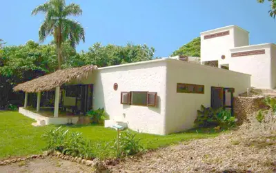 a small white house with a grass roof at La Cueva Eco-Lodge in Las Galeras