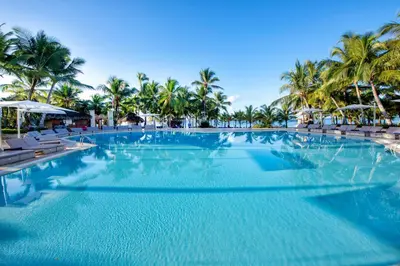 a large swimming pool with chairs and palm trees at Viva Dominicus Palace by Wyndham, A Trademark All Inclusive in Bayahibe