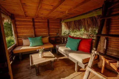 a porch of a wooden cabin with couches and a table at Ecolodge Tubagua Puerto Plata in Tubagua