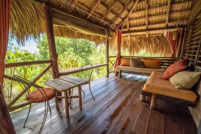 a porch of a hut with a bench and a table at Ecolodge Tubagua Puerto Plata in Tubagua