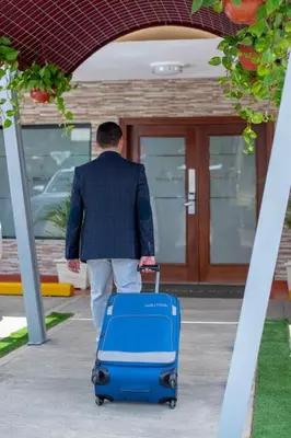 a man walking down a sidewalk with a blue suitcase at Hotel Real Bella Vista in Santo Domingo