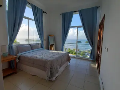 a bedroom with a bed and large windows at Hidden Paradise at Apto Del Cerro in Santa Bárbara de Samaná