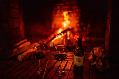 a bottle of wine and two wine glasses in front of a fireplace at Hotel Rancho Constanza & Cabañas de la Montaña in Constanza