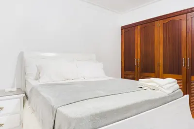 a white bedroom with a bed and a wooden cabinet at Apartamento Los Rieles in Santiago de los Caballeros
