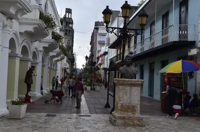 a street with people walking down a street with a statue at Hotel Cana Palma Zona Colonial in Santo Domingo
