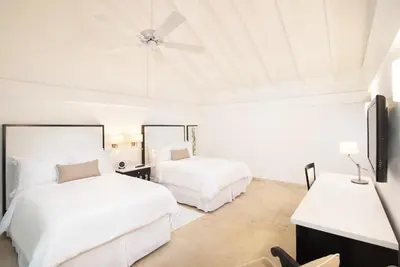 a white bedroom with two beds and a ceiling fan at Casa de Campo Resort & Villas in La Romana