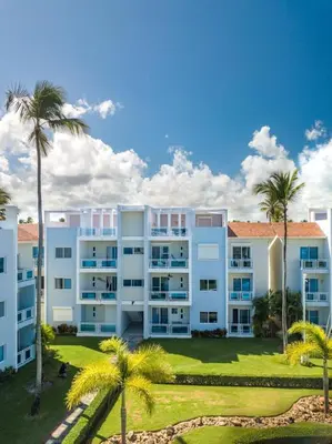 a large white building with palm trees in front of it at Caribbean Treasure in Punta Cana