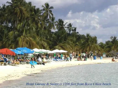 a beach with palm trees and people on the beach at Hotel Garant & Suites in Boca Chica