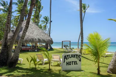 a hotel sign in front of a beach with palm trees at Hotel Atlantis in Las Terrenas