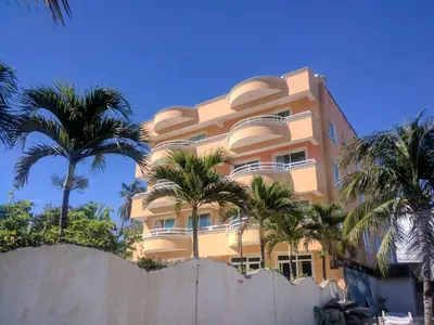 a tall building with palm trees in front of a fence at Aparta Hotel Caribe Paraiso in Juan Dolio