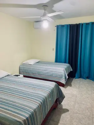 two beds in a room with blue curtains and a ceiling fan at Hotel Vista Sur in Los Patos