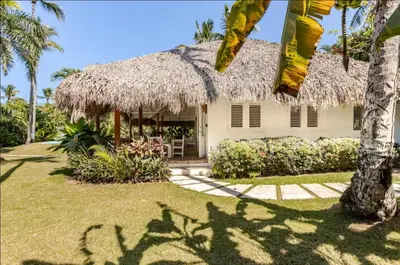 a house with a straw roof and a palm tree at Caribbean Beach Villa Playa Bonita Las Terrenas in Las Terrenas